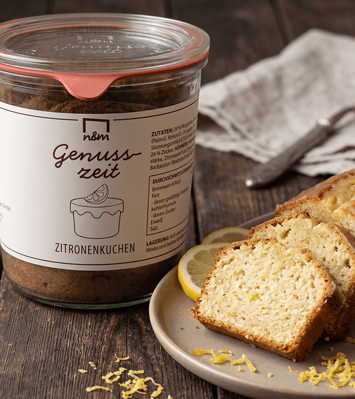Glas mit Zitronenkuchen-Backmischung und daneben auf einem Teller drei Scheiben Zitronenkuchen mit Zitronenscheiben.
