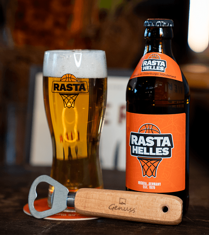 Bierflasche und Glas mit Rasta Helles Logo, daneben ein Flaschenöffner mit Holzgriff und "Genuss" graviert, auf dunklem Tisch.