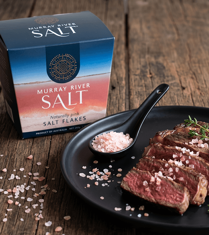 Packung Murray River pinke Salzflocken, daneben ein Teller mit geschnittenem Steak, bestreut mit Salzflocken und einem Löffel voll Salz.