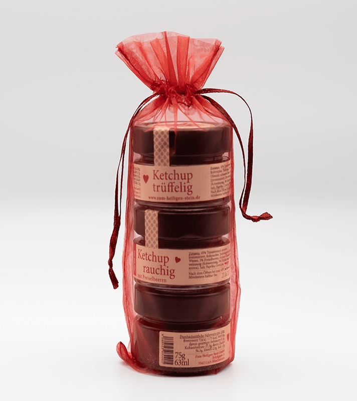 Drei kleine Gläser mit Ketchup in einem roten, durchsichtigen Beutel mit Zugband. Die Gläser sind beschriftet mit "Ketchup trüffelig" und "Ketchup rauchig".